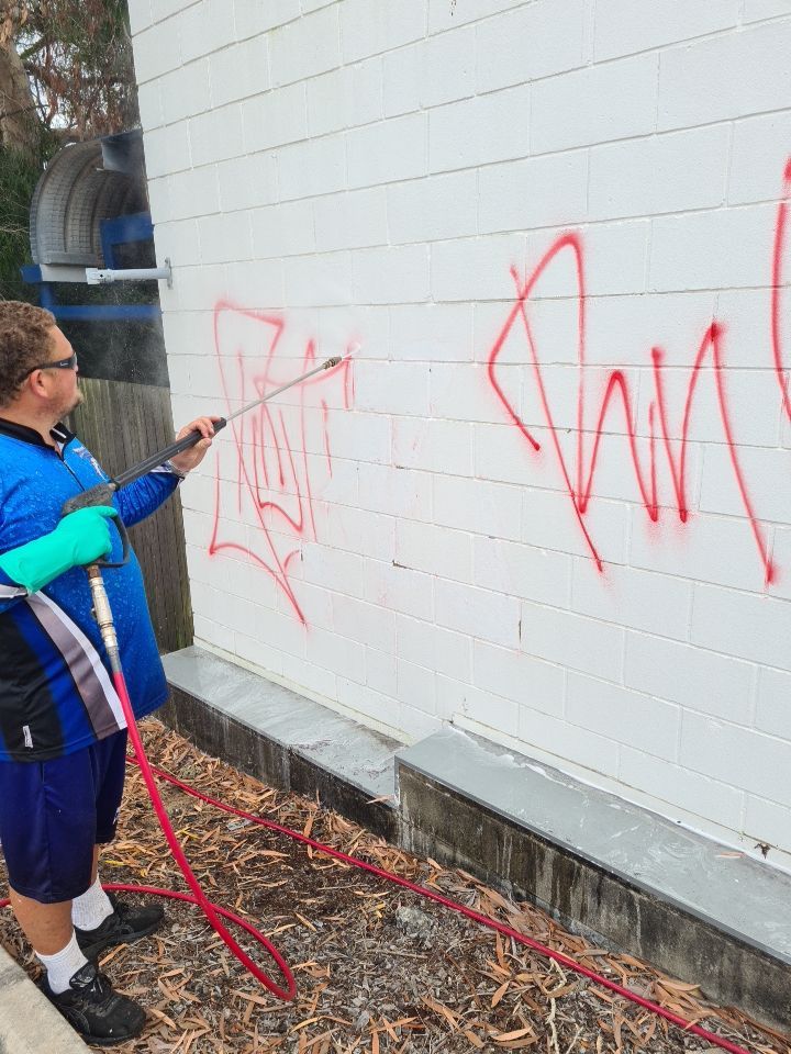 Graffiti cleaning - worker pressure washing graffiti off wall